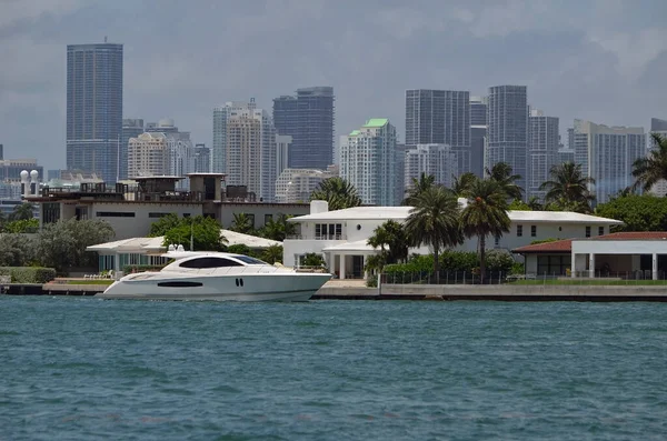 White motor yacht cruising by luxury real estate on RivoAlto island in Miami Beach with downtown tall building skyline in the background.