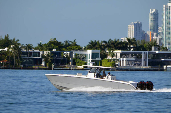 Рыбацкая лодка с четырьмя лодочными двигателями проплывает мимо роскошных домов на острове Магнолия, Майами-Бич, Флорида.