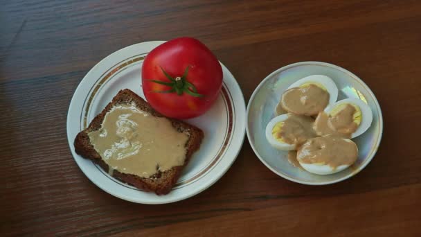 女性の手はごまバターとライ麦パンのスライスとトマトのプレートで覆われている卵プレートを奪う — ストック動画