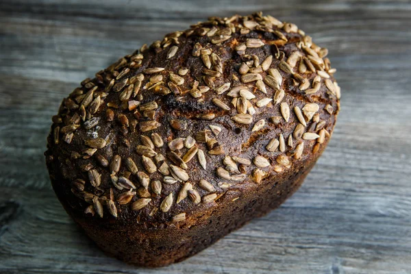 top view of whole tasty handmade rectangular black bread with sunflower seeds on top lie on dark wooden background