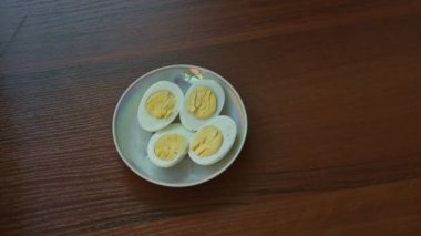 Kadın el ile haşlanmış yumurta dört yarısı kahverengi ahşap masa küçük tabakta kesiyor