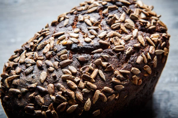 closeup top view of whole tasty homemade rectangular black bread with sunflower seeds on top lie on dark wooden background