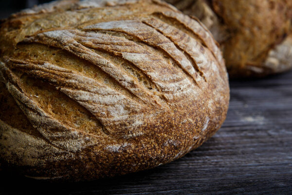 macro of whole homemade round white wheat bread lie on  dark wooden table