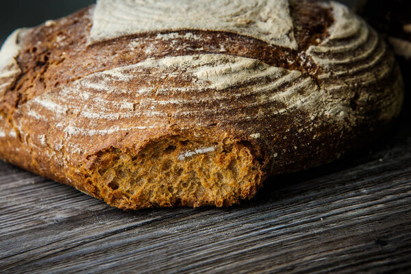 closeup big homemade textured round black piece of bread lie on dark wooden table