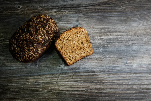 whole and half of handmade delicious handmade rectangular rye bread with sunflower seeds on dark table background
