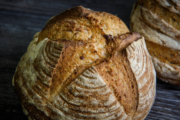 two whole homemade round white wheat bread lie on  dark wooden table