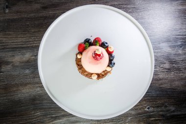 üstten görünüm üzerinde pembe tatlı taze ahududu ve ahşap masa arka plan üzerinde beyaz plaka üzerinde yaban mersini ile kaplı