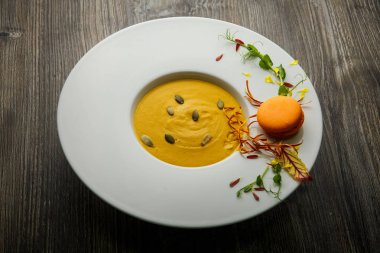 tohum ve turuncu acıbadem kurabiyesi dekorasyon ahşap arka plan üzerinde derin beyaz tabakta Taze kabak krem çorbası