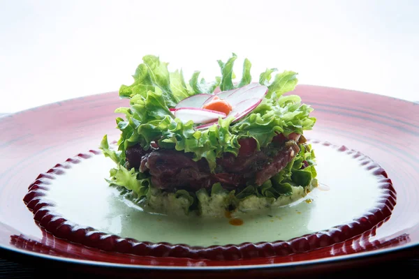 closeup salad with meat and flower topping made from radish on red plate against white background