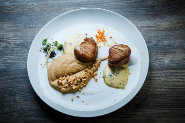 ızgara et püresi ve ahşap masa arka plan üzerinde beyaz Restoran tabakta sos ile iki lezzetli parça üzerinde üstten görünüm