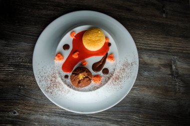 üstten görünüm lezzetli tatlı yuvarlak küçük pasta ve çikolata beyaz plaka üzerinde kırmızı vanilya sosu dekorasyonu ile