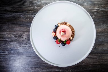üstten görünüm üzerinde pembe tatlı taze ahududu ve ahşap masa arka plan üzerinde beyaz plaka üzerinde yaban mersini ile kaplı