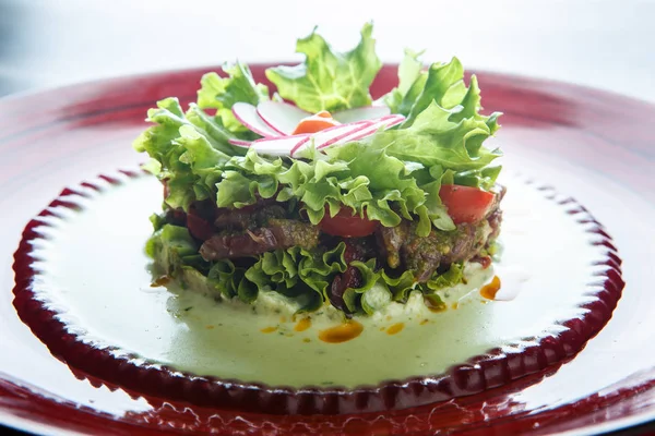 closeup salad with meat and flower topping made from radish on red plate against white background
