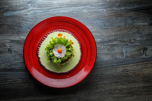 top view on healthy green salad with meat and flower decoration made from radish on red restaurant plate on wooden table
