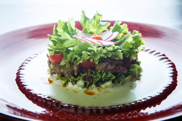 closeup salad with meat and flower topping made from radish on red plate against white background