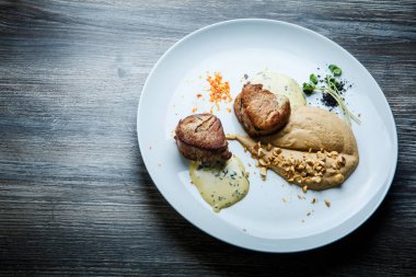 ızgara et püresi ve ahşap masa arka plan üzerinde beyaz Restoran tabakta sos ile iki lezzetli parça üzerinde üstten görünüm