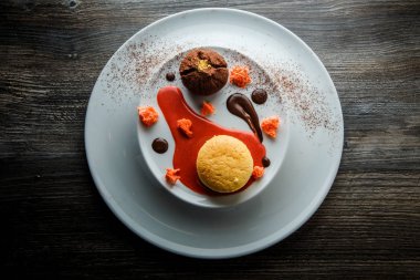 üstten görünüm lezzetli tatlı yuvarlak küçük pasta ve çikolata beyaz plaka üzerinde kırmızı vanilya sosu dekorasyonu ile