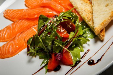 tatlı rucola ve domates salatası Somon dilimleri ile hizmet ve ekmek gri tablo arka plan üzerinde beyaz Restoran plaka stand