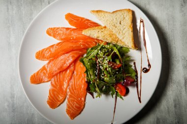 Somon dilimleri üzerinde üstten görünüm rucola ile hizmet ve domates salatası ve beyaz Restoran plaka üzerinde kızarmış ekmek gri tablo arka plan üzerinde durmak