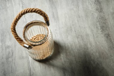 Üstten Görünüm açılan cam kavanoz buğday tohumu ve ip işleyici ile gri masada duruyor