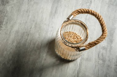 Üstten Görünüm açılan cam kavanoz buğday tohumu ve ip işleyici ile gri masada duruyor
