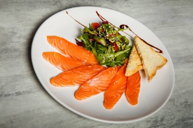 Somon dilimleri ile rucola hizmet ve domates salatası ve beyaz Restoran plaka üzerinde kızarmış ekmek gri tablo arka plan üzerinde durmak