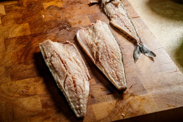 three divided part of raw mackerel fillet with bones lie on wooden tray on kitchen table