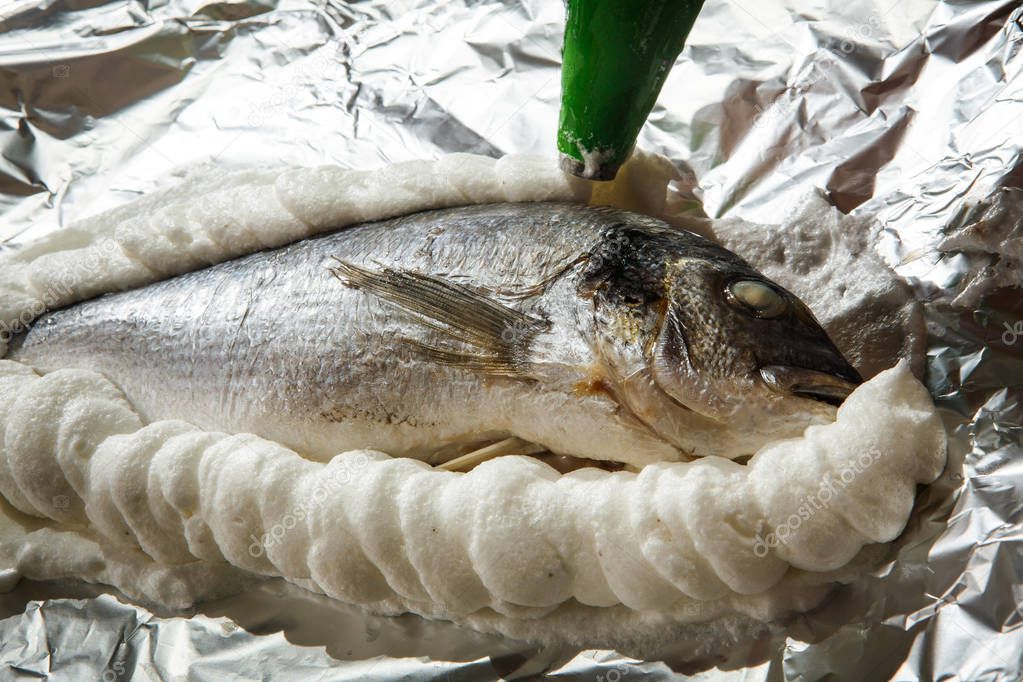 covering dorado stuffed with herbs on foil with whipped egg whites with salt
