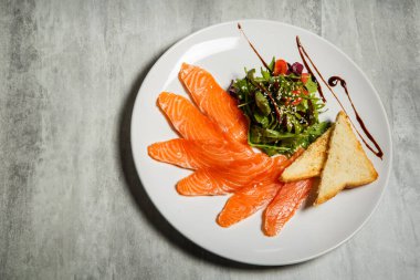 Somon dilimleri üzerinde üstten görünüm rucola ile hizmet ve domates salatası ve beyaz Restoran plaka üzerinde kızarmış ekmek gri tablo arka plan üzerinde durmak
