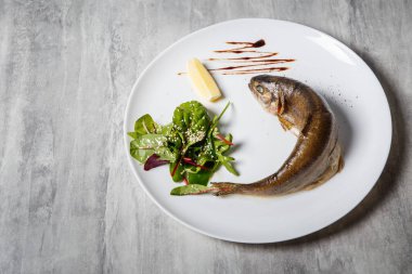 Fırında Alabalık rukola salata, limon ve beyaz Restoran plaka gri tablo üzerinde sos ile servis üstten görünüm