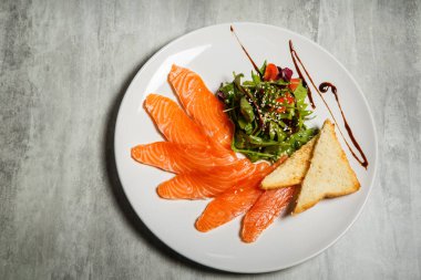 Somon dilimleri üzerinde üstten görünüm rucola ile hizmet ve domates salatası ve beyaz Restoran plaka üzerinde kızarmış ekmek gri tablo arka plan üzerinde durmak