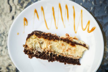Yukarıdan küçük parçası cheesecake ile çikolata karamel sulama ile beyaz plaka üzerinde yatıyor