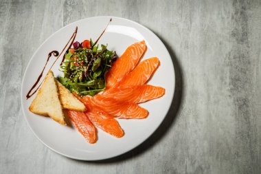 Somon dilimleri ile rucola hizmet ve domates salatası ve beyaz Restoran plaka üzerinde kızarmış ekmek gri tablo arka plan üzerinde durmak