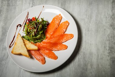 Somon dilimleri üzerinde üstten görünüm rucola ile hizmet ve domates salatası ve beyaz Restoran plaka üzerinde kızarmış ekmek gri tablo arka plan üzerinde durmak