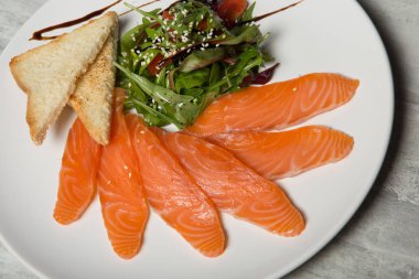 closeup Somon dilimleri ile rucola hizmet ve domates salatası ve beyaz Restoran plaka üzerinde kızarmış ekmek gri tablo arka plan üzerinde durmak