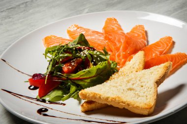 Somon dilimleri ile rucola hizmet ve domates salatası ve beyaz Restoran plaka üzerinde kızarmış ekmek gri tablo arka plan üzerinde durmak