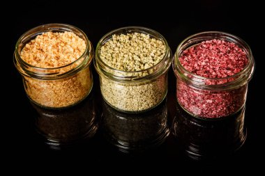 Üç küçük cam kavanoz siyah ayna arka plan üzerinde pembe, sarı, turuncu, yeşil ve kırmızı renkli deniz tuzu ile dolu