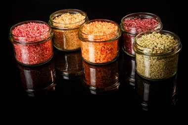 beş küçük cam kavanoz siyah ayna arka plan üzerinde pembe, sarı, turuncu, yeşil ve kırmızı renkli deniz tuzu ile dolu