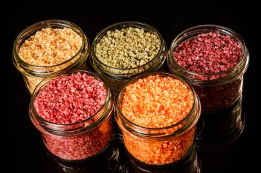 siyah ayna arka plan üzerinde pembe, sarı, turuncu, yeşil ve kırmızı renkli deniz tuzu ile dolu tatlı küçük cam kavanoz