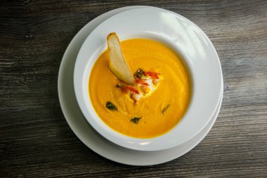 üstten görünüm krem balık çorbası karides kuyrukları ve bir dilim kuru ekmek ile dekore edilmiş ahşap masa derin beyaz Restoran tabakta servis
