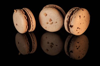 Üç bej fıstık macaroons çikolata dolgulu siyah ayna arka plan yansıması ile servis