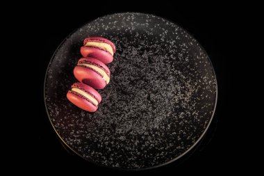 üstten görünüm üç barry macaroons sarı vanilya dolgulu siyah arka plan üzerine siyah dokulu tabakta servis