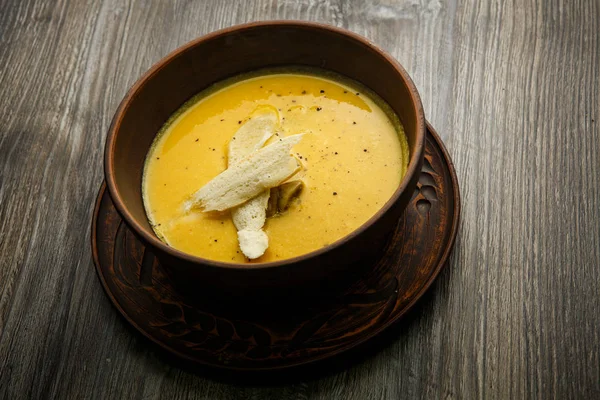 Yellow cream soup decorated with mushrooms and two slices of dried bread served in deep clay plate on wooden table — Stock Image Yellow Cream Soup Decorated Mushrooms Two Slices Dried Bread Served Royalty Free Stock Images