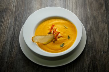 ahşap masa üzerinde derin beyaz Restoran tabak karides kuyrukları ve bir dilim kuru ekmek ile dekore edilmiş taze balık krem çorba servis