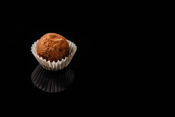 Крупный план полезных органических круглых шоколадных конфет ручной работы, украшенных коричневым какао порошком на черном фоне зеркала
