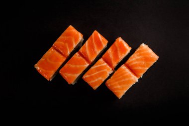 kırmızı sos siyah arka plan üzerine hizmet üstten görünüm philadelphia rulo suşi somon füme, salatalık ve krem peynir ile süslenmiş