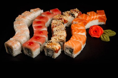 çeşitli philadelphia suşi rulo ile somon, yılan balığı, ton balığı ve kaplan karides kırmızı zencefil siyah arka plan üzerine servis yapılan çiçek ile dekore edilmiş