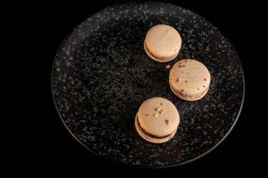 en iyi çikolata dolgulu siyah arka plan üzerine siyah dokulu tabakta servis üç bej macaroons görüntülemek