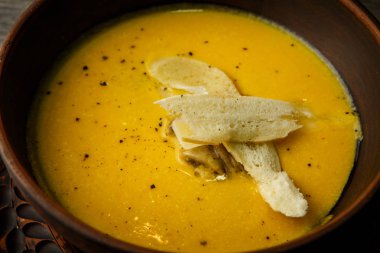 portre sarı krem çorba mantar ve iki dilim kuru ekmek ile dekore edilmiş ahşap masa derin kil tabakta servis