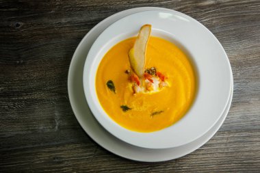 üstten görünüm sarı krem çorba karides kuyrukları ve bir dilim kuru ekmek ile dekore edilmiş ahşap masa derin beyaz Restoran tabakta servis